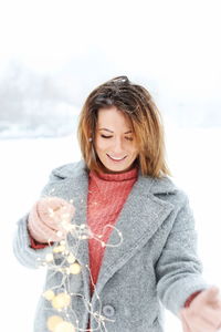 Young woman holding illuminated string lights while standing on snow covered field