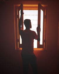 Rear view of silhouette man standing against window at home