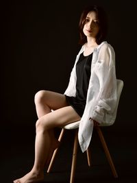 Portrait of young woman standing against black background