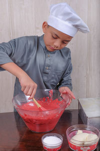 Boy mixing batter in bowl on table at home