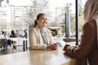 Happy businesswoman talking with colleague sitting at table in coffee shop