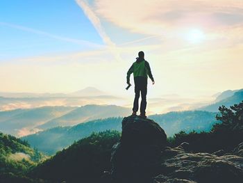 Man standing on rock looking at mountains against sky