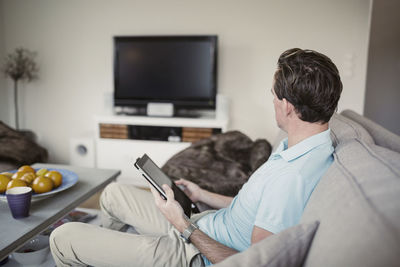 Side view of man with digital tablet sitting on sofa at home