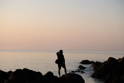 People standing on rock by sea against sky during sunset