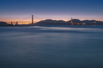 View of suspension bridge over river at sunset