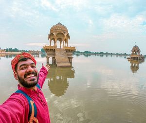 Portrait of man gesturing on built structure in lake