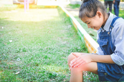 Side view of girl looking at knee while sitting on field