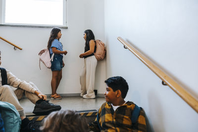 Female friends talking with each other near wall in school