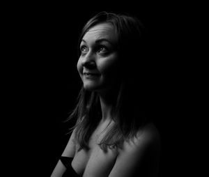 Portrait of young woman looking away against black background