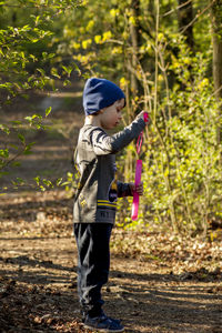 A pretty boy on a walk in the woods, wearing a blue cap and a gray sweater, blowing soap bubbles. 