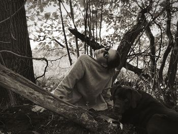 Portrait of woman sitting with dog on tree trunk in forest