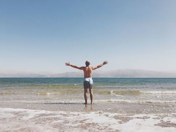 Rear view of woman standing on beach against clear sky