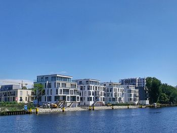 Buildings by river against clear blue sky