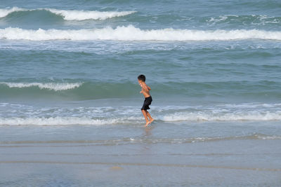 Side view of shirtless boy jumping over wave at beach