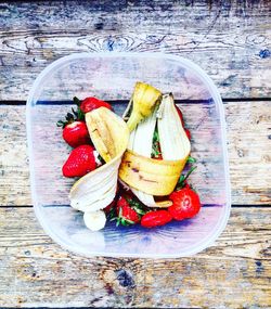 Directly above shot of banana peels with strawberries in bowl on table