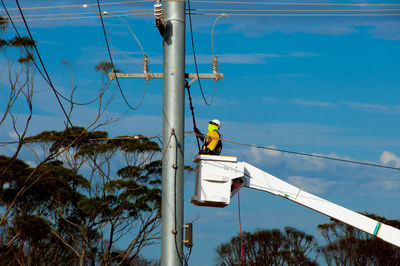 Man working on electrical pole against sky