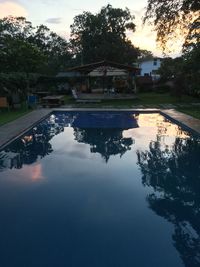 Reflection of silhouette trees in swimming pool against sky