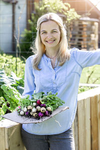 Portrait of mid adult woman holding radishes at farm