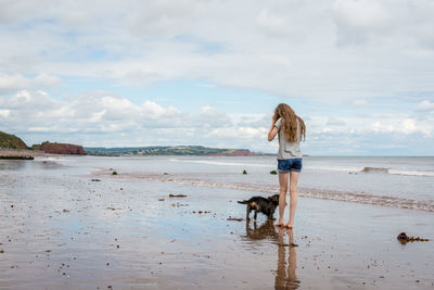 Rear view of girl with dog standing on shore at beach