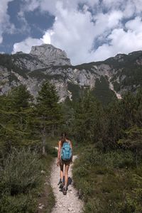 Rear view of woman walking on footpath against mountain and sky