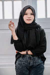 Portrait of young woman standing against wall