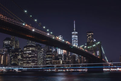 Low angle view of illuminated brooklyn bridge over east river against sky at night