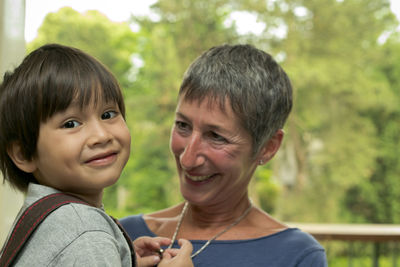 Portrait of smiling grandson with grandmother against trees