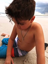 Close-up of shirtless boy sitting on sand at beach
