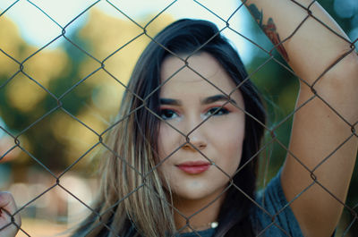 Portrait of beautiful young woman standing by fence