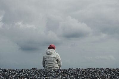 Rear view of woman sitting on hill against cloudy sky