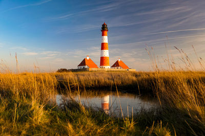 Lighthouse on field by building against sky