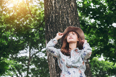 Low angle view of young woman against tree trunk