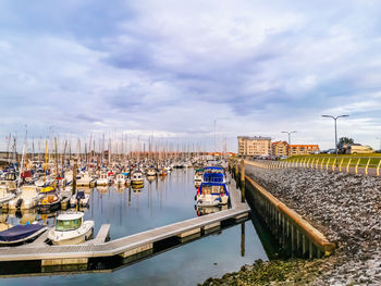 Sailboats moored at harbor in city against sky