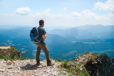 Side view of mid adult man with backpack standing on mountain against sky