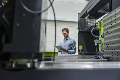 Businessman in high tech company controlling manufacturing machines, using digital tablet