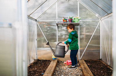 Young boy watering seeds in backyard greenhouse during spring time