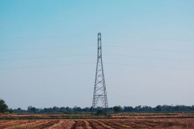 Low angle view of electricity pylon on field against clear sky