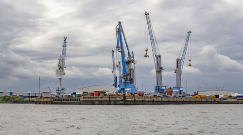 Cranes at commercial dock against sky