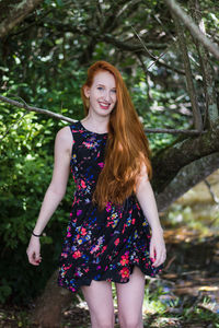 Portrait of beautiful young woman standing against trees