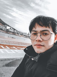 Portrait of young man wearing eyeglasses against sky