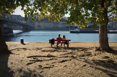 Rear view of couple sitting on bench at danube riverbank in park