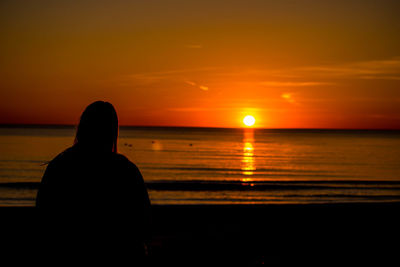 Rear view of silhouette man on beach against sky during sunset
