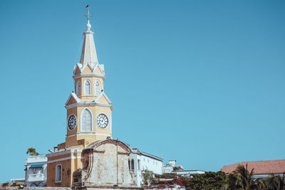 Low angle view of clock tower amidst buildings against clear blue sky