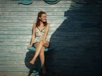 Young woman wearing sunglasses sitting on table against blue wooden wall