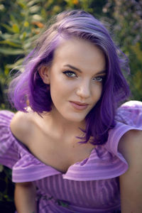 Portrait of a teenage girl with purple hair and an earring in her nose lying in the grass in nature