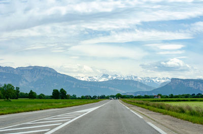 Empty road along landscape against mountains and sky