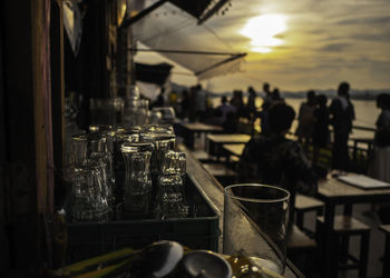 Glasses in container with people in background at restaurant during sunset