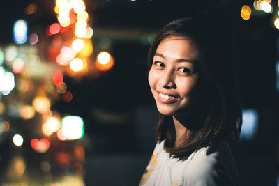 Portrait of smiling young woman at illuminated christmas tree
