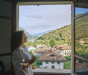 Mature woman with coffee cup looking out from window