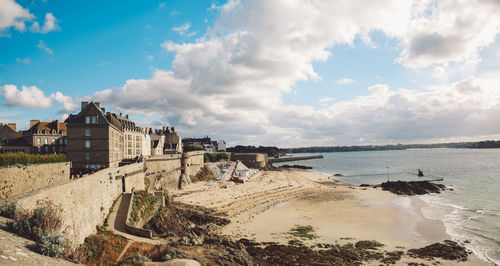 Scenic view of beach by buildings against cloudy sky